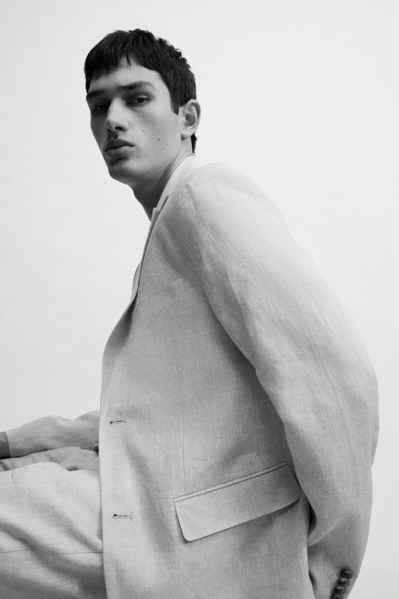 Close-up monochrome portrait of a male model wearing a light tailored suit against a plain background for H&M.