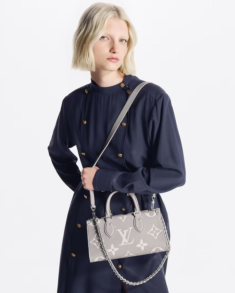 Model wearing a dark blue buttoned dress holding a grey patterned handbag against a white background