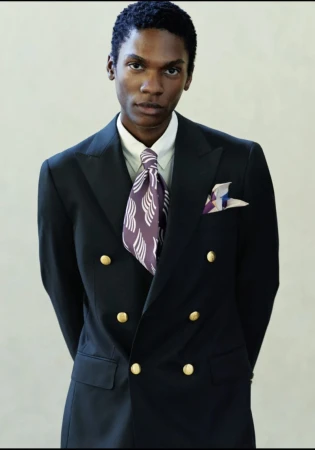 Elegant adult Black male in double-breasted navy suit, gold buttons, patterned tie and pocket square, eye-level indoor studio portrait.