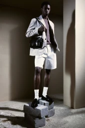 Model Nonso Ojukwu wearing a light blazer, white shorts, and loafers, standing on stone blocks for H&M Spring.