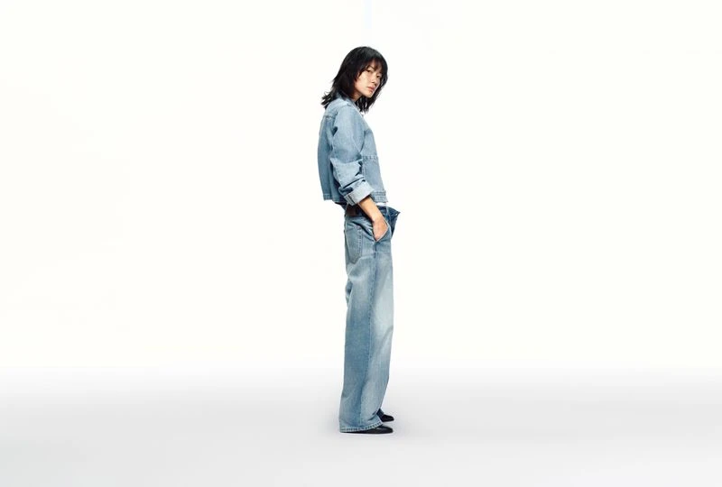 Asian woman poses in light-blue denim jacket and wide-leg jeans against a white backdrop in a fashion studio shot, showcasing material and cut.