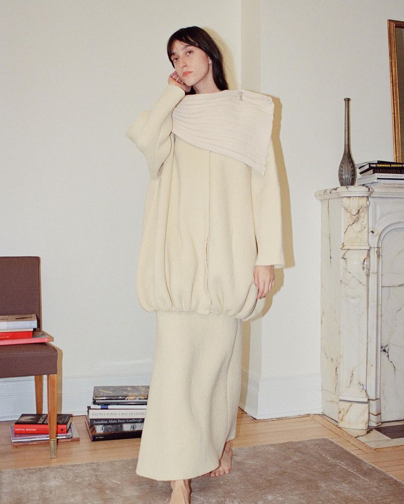 Adult female in a cream-colored outfit posing indoors. Neutral tones and soft lighting create a calm atmosphere in a studio setting.