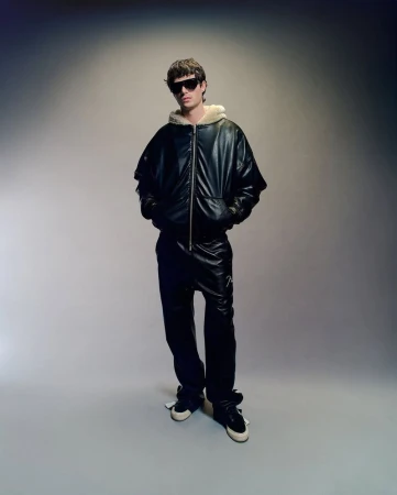Full-length shot of adult male model wearing a black leather bomber jacket with sunglasses in a photo studio setting.