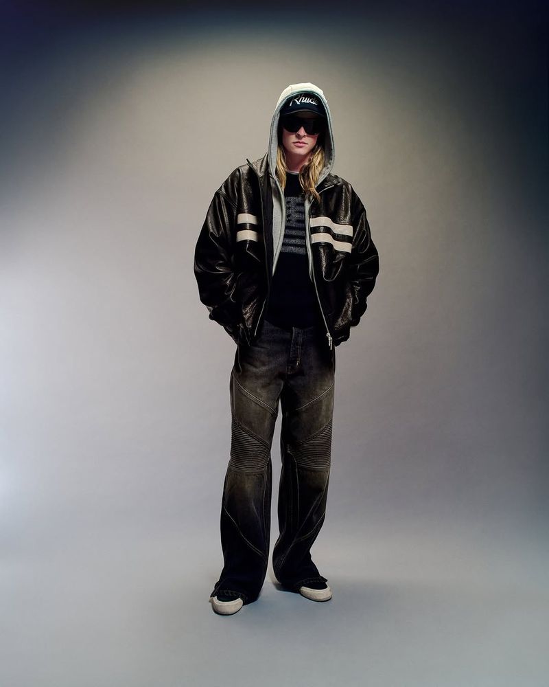 Adult male with blonde hair and sunglasses poses wearing a hooded jacket, t-shirt, baggy jeans, and sneakers in a studio setting.