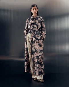 Model standing in a floral patterned trench coat and trousers against a dark brushed metallic background