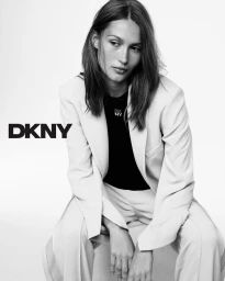 Model Vika Evseeva seated in a light-coloured trouser suit against a plain white studio background for DKNY