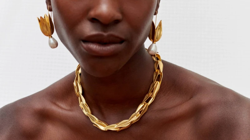 Close-up portrait of a woman wearing sculptural gold leaf necklace and matching drop earrings with pearl pendants for Oroton.