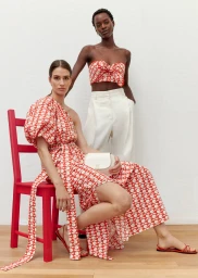Two female models showcasing Oroton Resort Collection 24 apparel, featuring red patterned clothing and a white handbag against a white background.