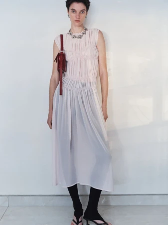 Model wearing a pleated pale pink sleeveless dress and carrying a burgundy shoulder bag against a light background