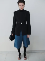 Model wearing structured black blazer, blue denim shorts, and black handbag against a neutral wall