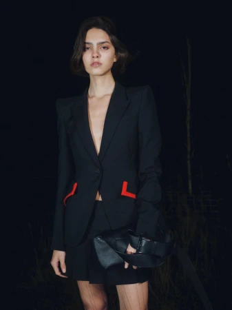 Model in a black blazer with red pocket accents wearing a black skirt against a dark outdoor night background