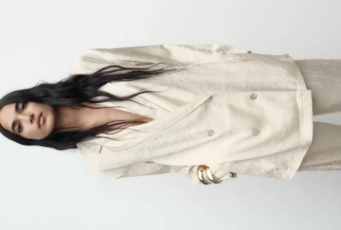 Model wearing a cream double breasted blazer and matching trousers against a neutral white background