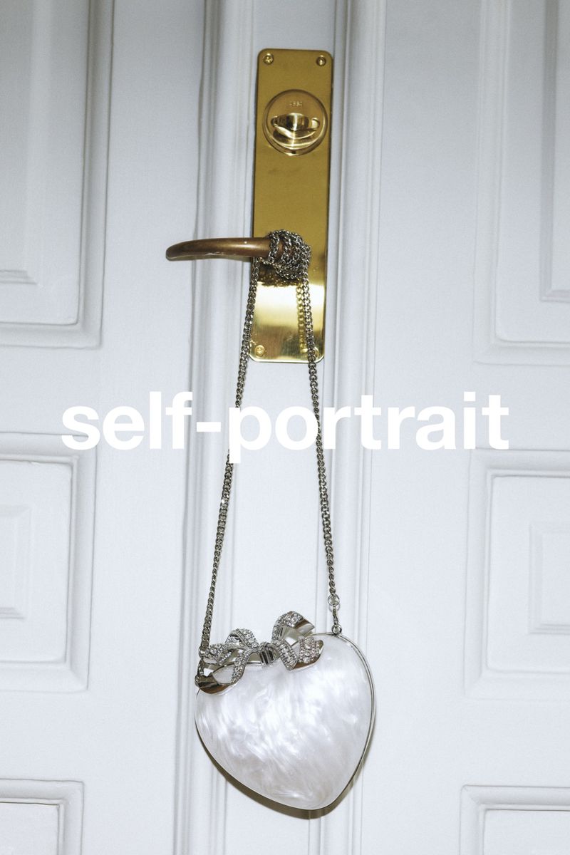 White marbled heart-shaped handbag hanging by a silver chain from a brass door handle against a white paneled door