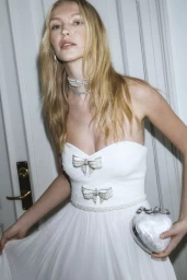 Model wearing a white strapless bow-embellished dress holding a heart-shaped bag for Self-Portrait S/S 2025