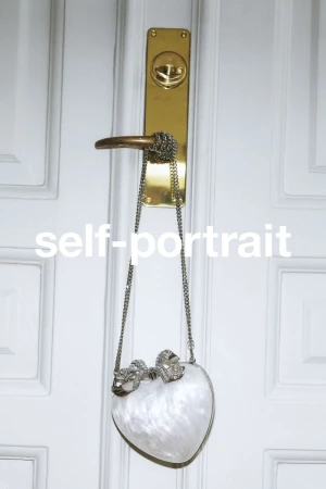 White marbled heart-shaped handbag hanging by a silver chain from a brass door handle against a white paneled door