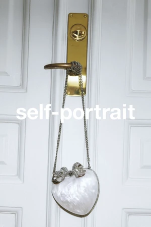 White marbled heart-shaped handbag hanging by a silver chain from a brass door handle against a white paneled door