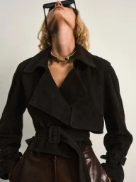 Model wearing dark sunglasses and a black belted jacket looking upward against a plain white background for Nour Hammour Spring Summer 25.