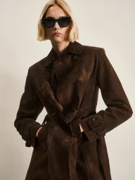 Model wearing dark sunglasses and a brown coat against a light studio backdrop for Nour Hammour Spring Summer 25.