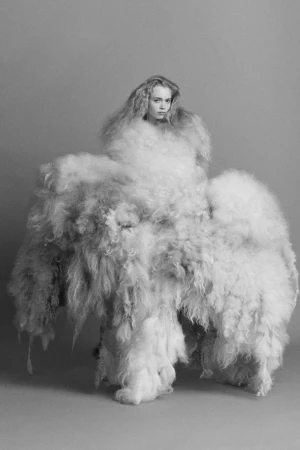 Monochrome studio shot of a woman enveloped in large, shaggy material, creating a striking visual effect, neutral grey backdrop.