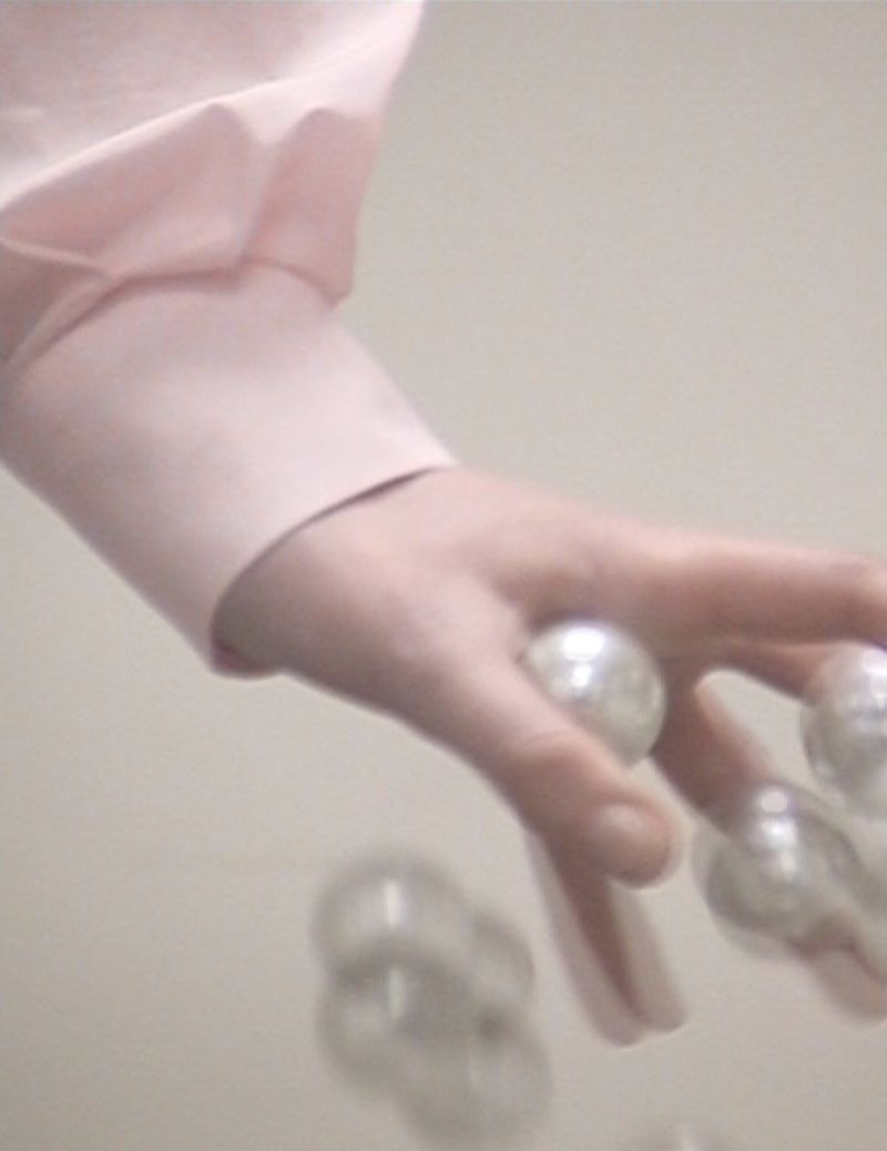 Close-up of a hand in a light pink shirt with several white, shiny, round pearls falling out of the palm on a white background.