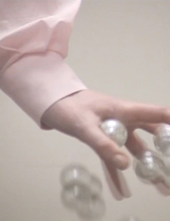 Close-up of a hand in a light pink shirt with several white, shiny, round pearls falling out of the palm on a white background.