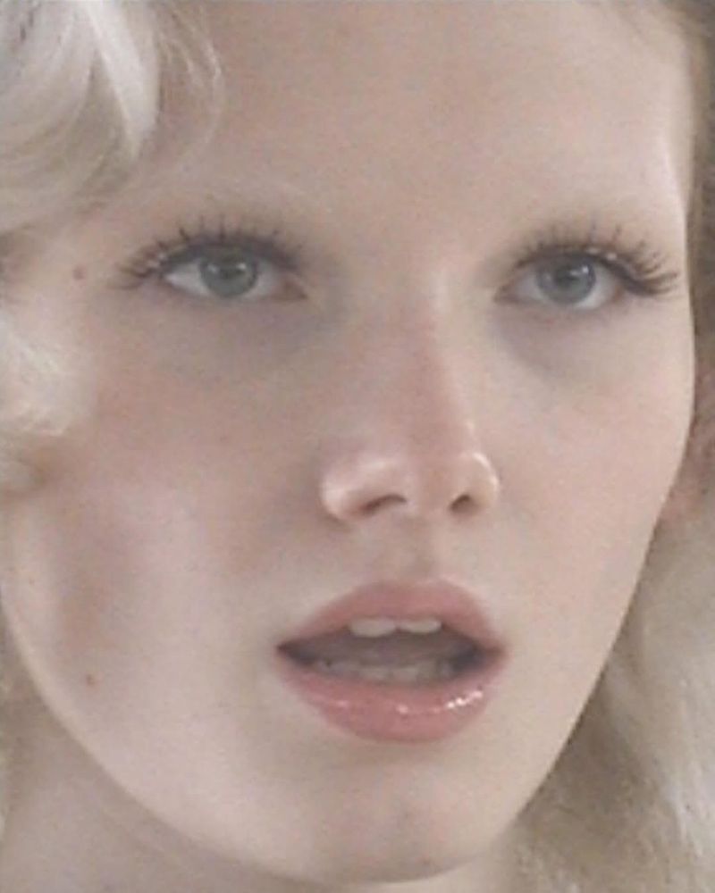 Close-up portrait of a fair-skinned adult woman with light blonde hair, featuring her eyes, nose, and mouth, set against a soft, diffused backdrop.