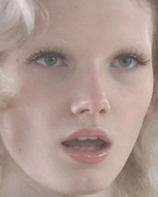 Close-up portrait of a fair-skinned adult woman with light blonde hair, featuring her eyes, nose, and mouth, set against a soft, diffused backdrop.