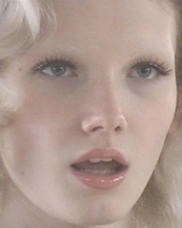 Close-up portrait of a fair-skinned adult woman with light blonde hair, featuring her eyes, nose, and mouth, set against a soft, diffused backdrop.