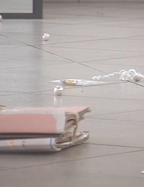 Close-up of scattered crumpled paper balls, a stack of documents, and spilled white substance on a light gray tiled floor indoors.