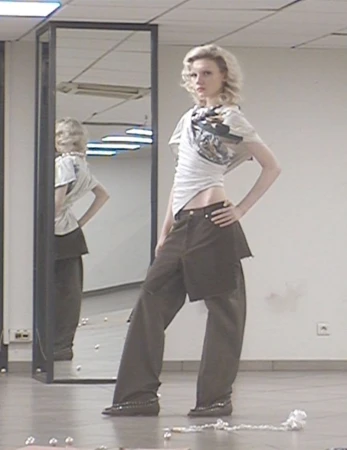 A slender fashion model poses in a casual outfit in an indoor setting, reflected in a mirror behind, accented by scattered pearls.