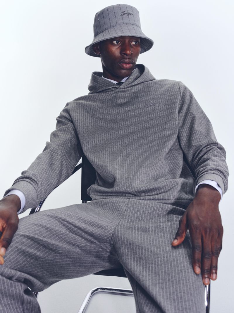 Adult male model in a matching grey pinstripe bucket hat, hoodie, and pants, seated against a neutral background in a studio shot.