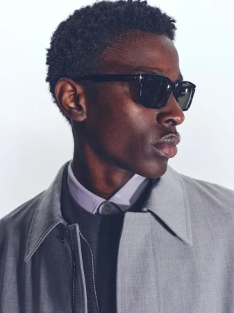 Close-up portrait of a black man wearing black sunglasses and a grey coat for BOSS Spring 2025 Menswear.