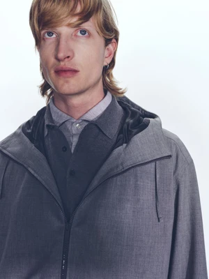Close-up portrait of a male model wearing a grey hooded zip jacket over a collared shirt against a white background