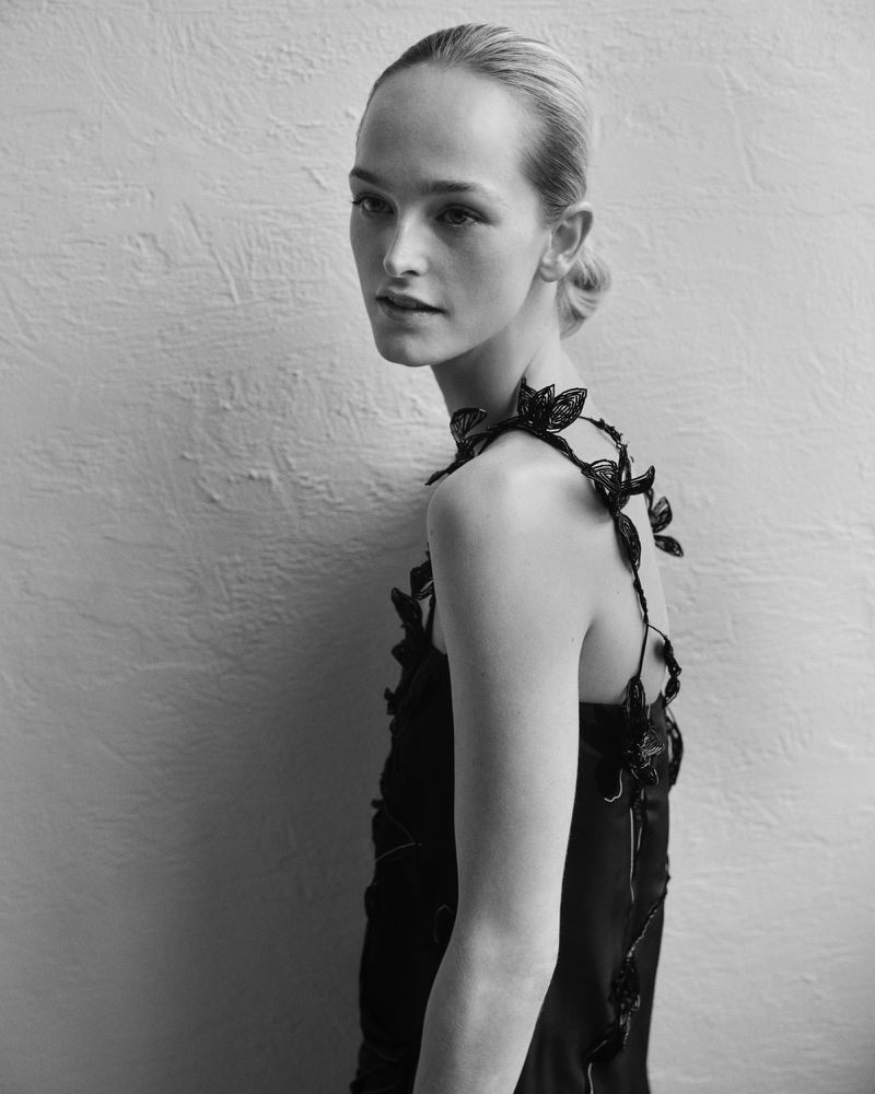 Model Jean Campbell wearing a black embellished strap dress against a textured light wall for Giada F/W 25.