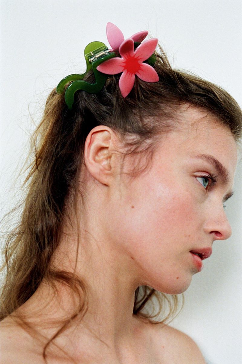 Profile shot of a woman with a pink flower hair clip, showcasing fashion, beauty and accessory, and studio setting with soft lighting.