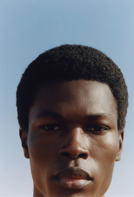 Close-up portrait of an African American adult male with short dark hair against a clear blue sky. Head and shoulders, direct gaze.