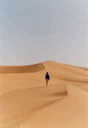 A lone figure walking across sweeping sand dunes under an overcast sky for Zara Man Spring 2025 campaign.