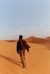 Model walking across expansive sand dunes under a clear sky for Zara Man Spring 2025 campaign