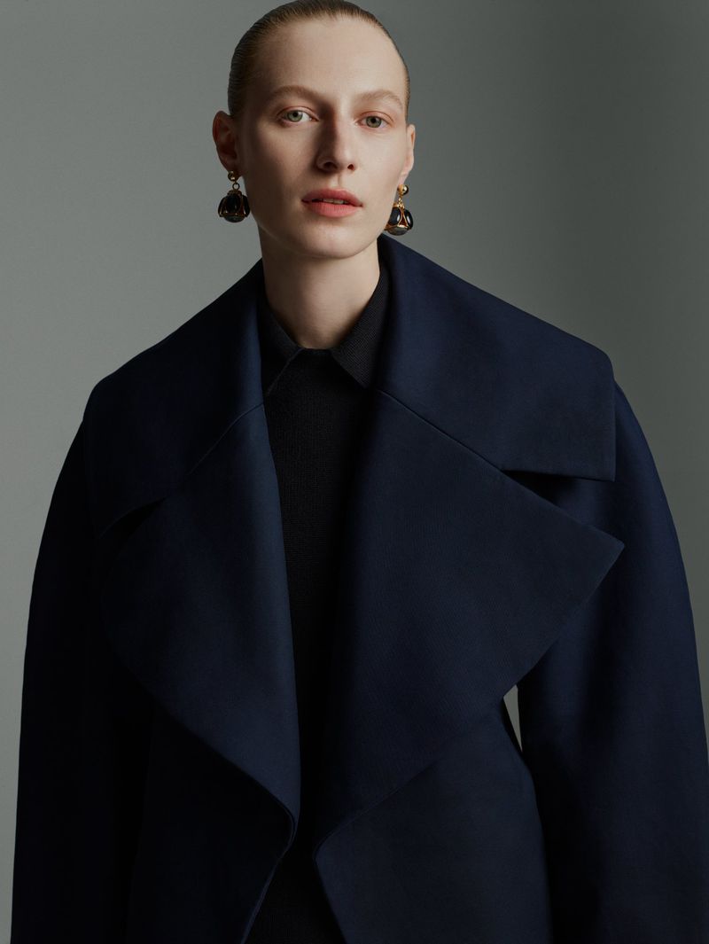Woman in navy coat and earrings, studio shot. Portrait of a model in a fashion coat with earrings in a photography studio.