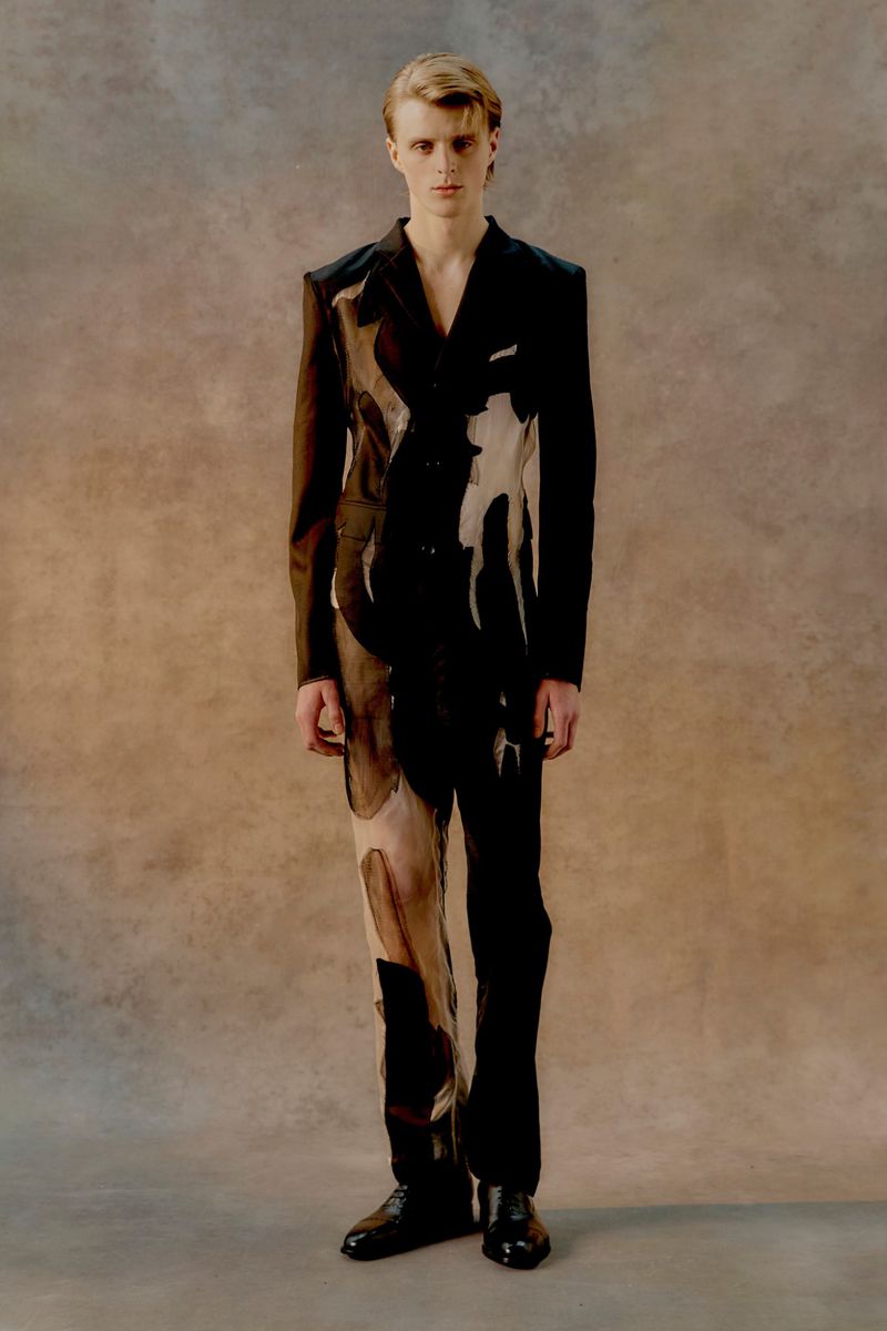 Fashionable young adult posing in an abstract black and tan suit against a neutral background in a full-length portrait shot.