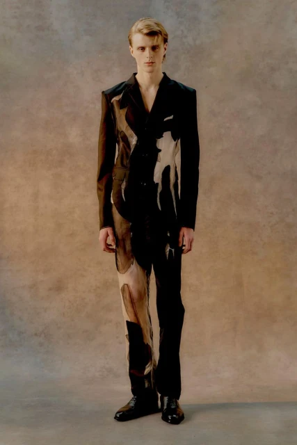 Fashionable young adult posing in an abstract black and tan suit against a neutral background in a full-length portrait shot.