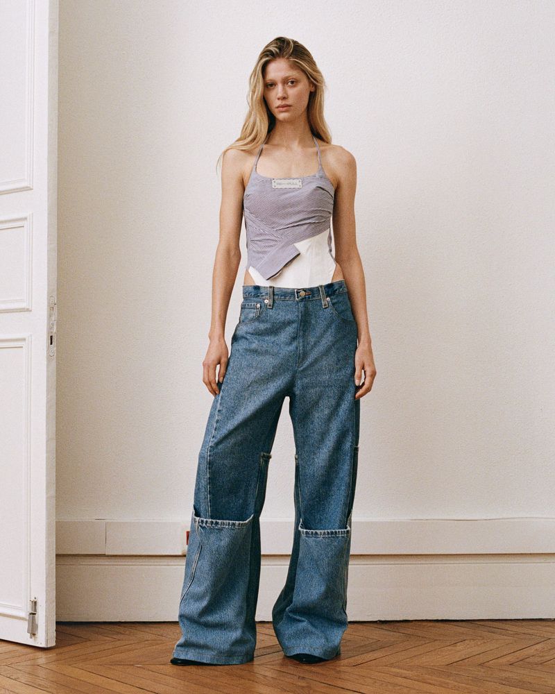 Model wearing a layered halter top and wide-leg denim jeans standing in a bright room with parquet flooring.
