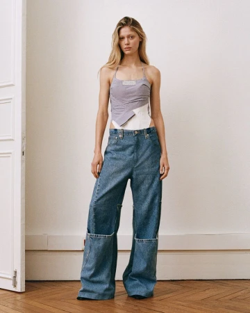 Model wearing a layered halter top and wide-leg denim jeans standing in a bright room with parquet flooring.