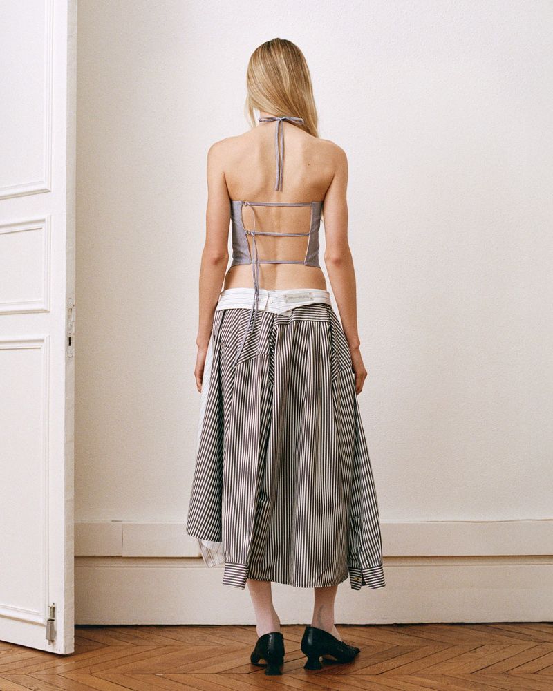 Model from behind wearing a strappy backless top and layered striped skirt standing indoors