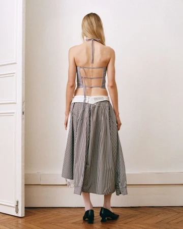 Model from behind wearing a strappy backless top and layered striped skirt standing indoors