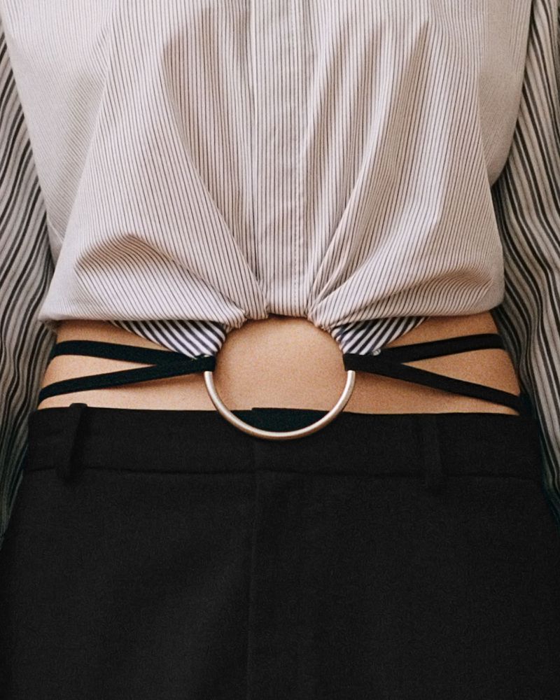 Fashionable torso shot featuring a woman in a striped blouse, with a metallic ring detail showing a glimpse of skin above black pants.
