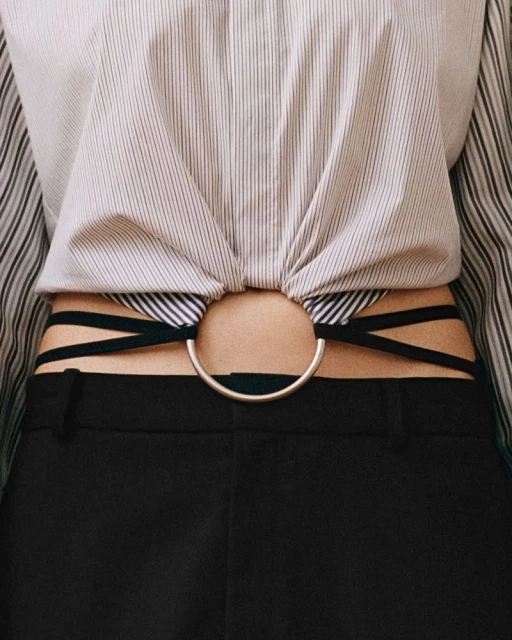 Fashionable torso shot featuring a woman in a striped blouse, with a metallic ring detail showing a glimpse of skin above black pants.