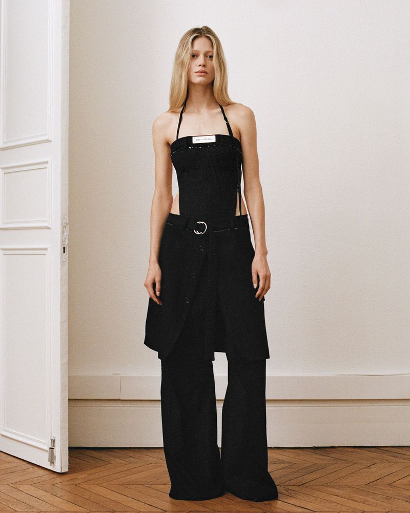 Elegant, full-length shot of a blonde woman in a modern halter top and wide-leg pants, posing in a minimally decorated interior space.