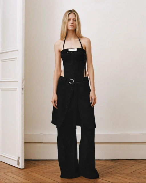Elegant, full-length shot of a blonde woman in a modern halter top and wide-leg pants, posing in a minimally decorated interior space.