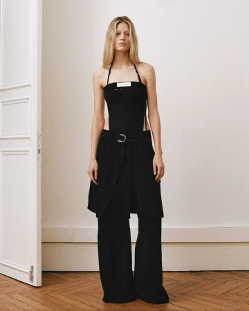 Elegant, full-length shot of a blonde woman in a modern halter top and wide-leg pants, posing in a minimally decorated interior space.